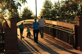 A picture of a family walking across a wooden bridge in a park.